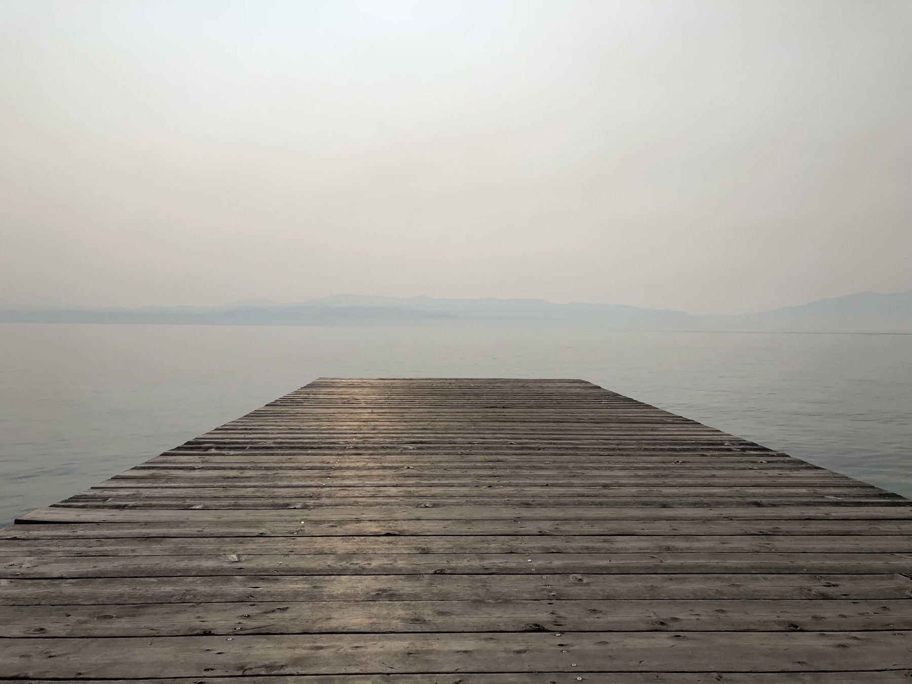 A wooden dock reaching into a calm, hazy lake